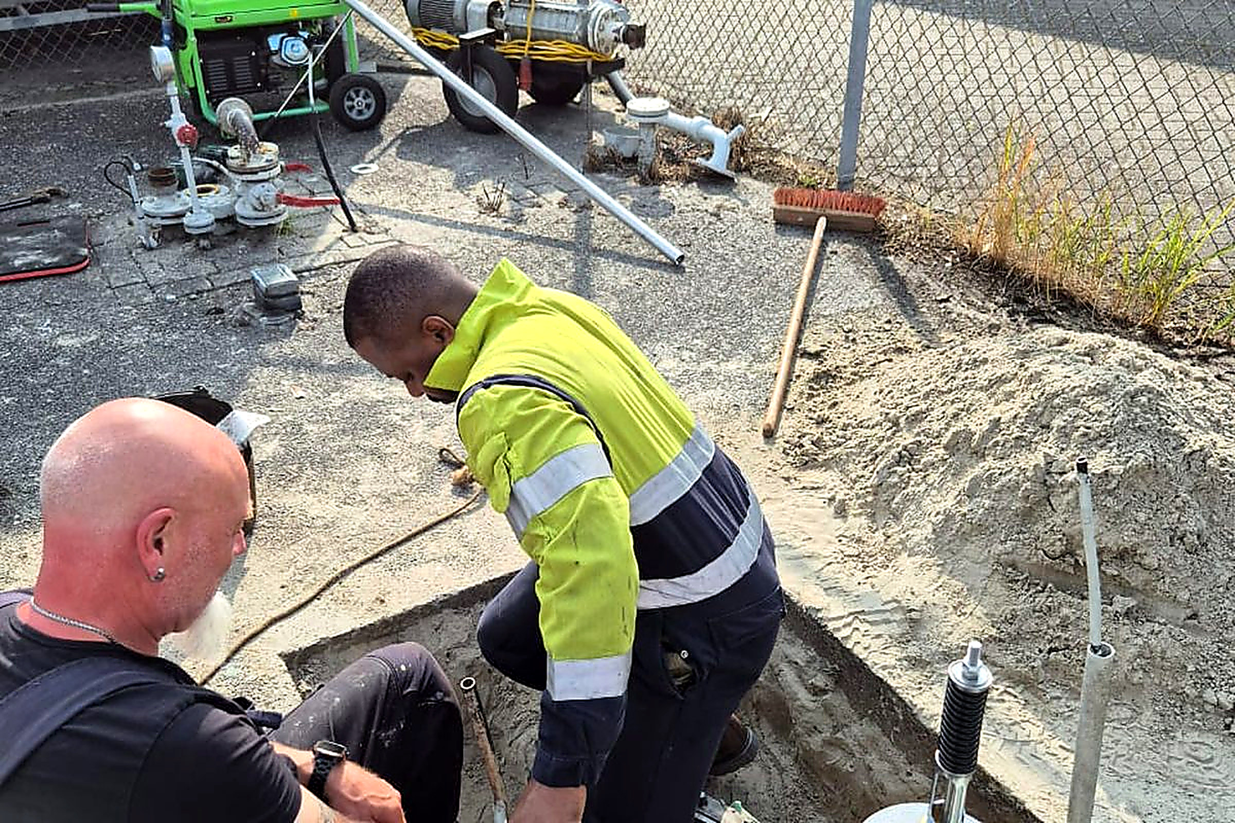 Two Bomart technicians performing on-site equipment maintenance, one wearing a hi-viz safety vest